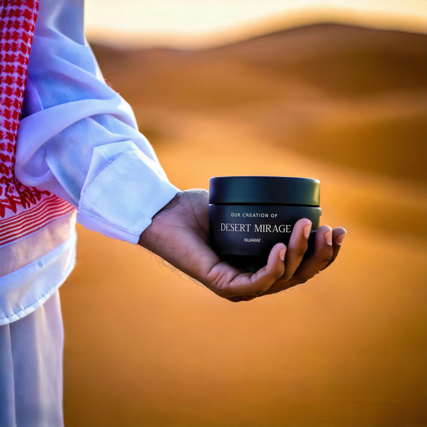 A person in traditional Middle Eastern attire holding a Nuarai® Desert Mirage bakhoor jar against the backdrop of golden sand dunes, symbolizing luxury, warmth, and inspiration from Louis Vuitton Ombre Nomade.